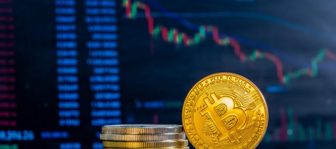 Close-up of golden Bitcoins on a dark reflective surface and the histogram of decreasing crypto in the background
