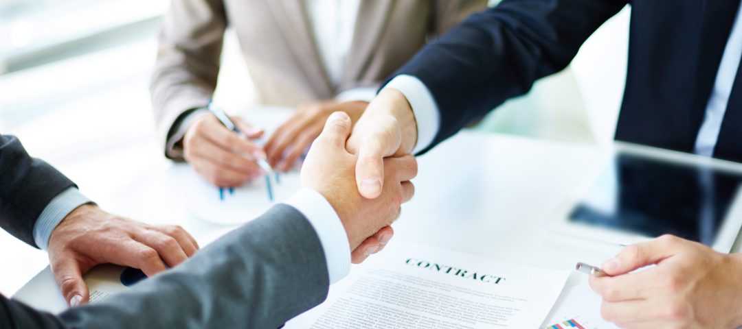 Image of business partners handshaking over business objects on workplace